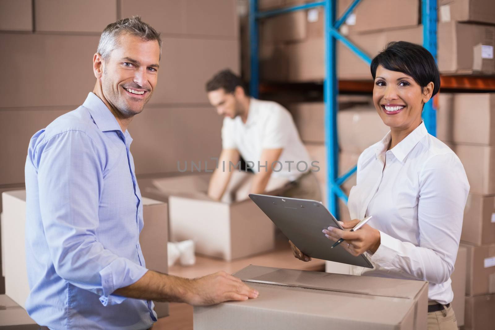 Warehouse manager writing on clipboard talking to colleague in a large warehouse