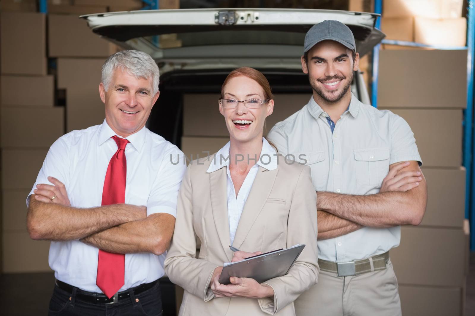 Warehouse managers and delivery driver smiling at camera in a large warehouse