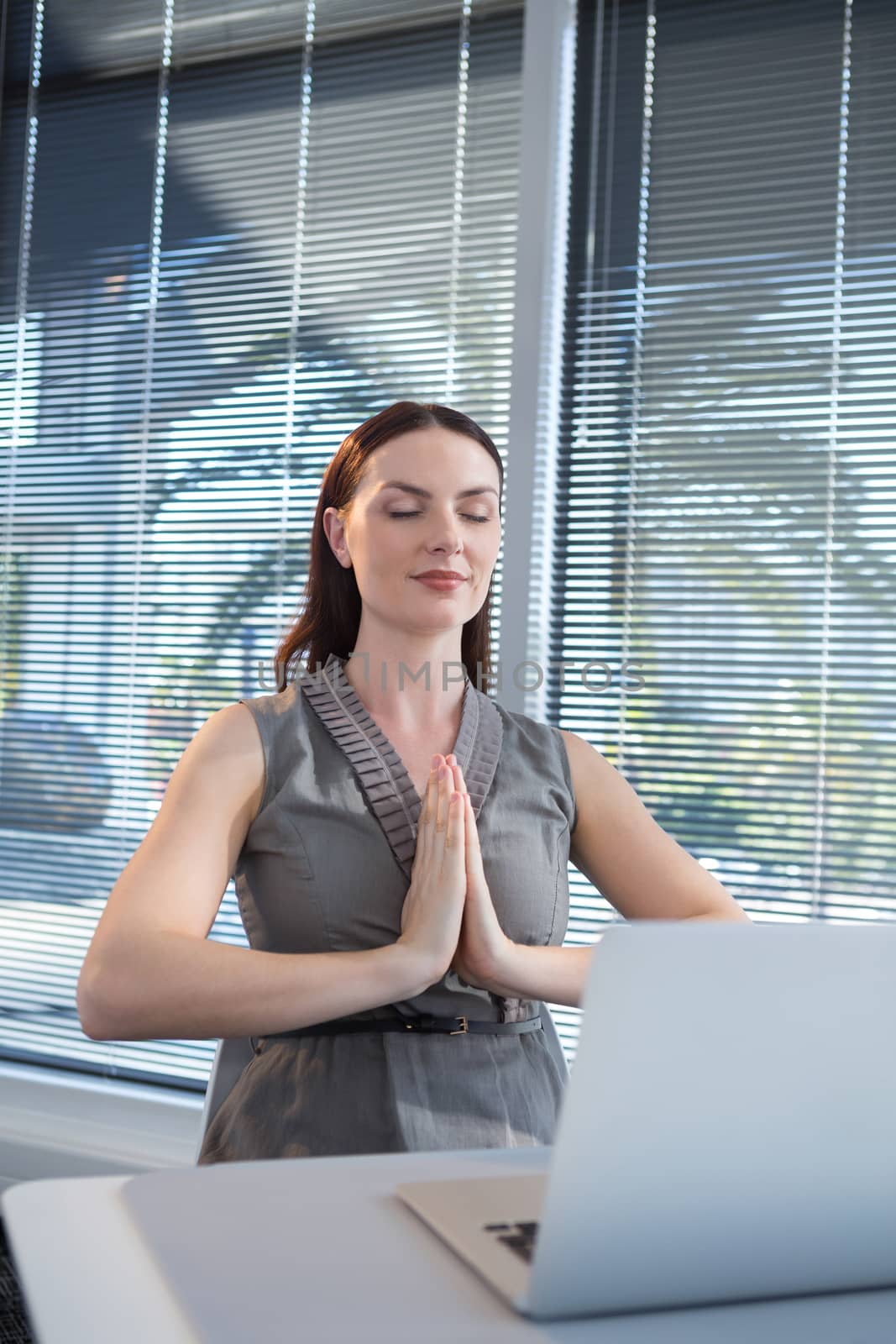 Female executive performing yoga at desk in office