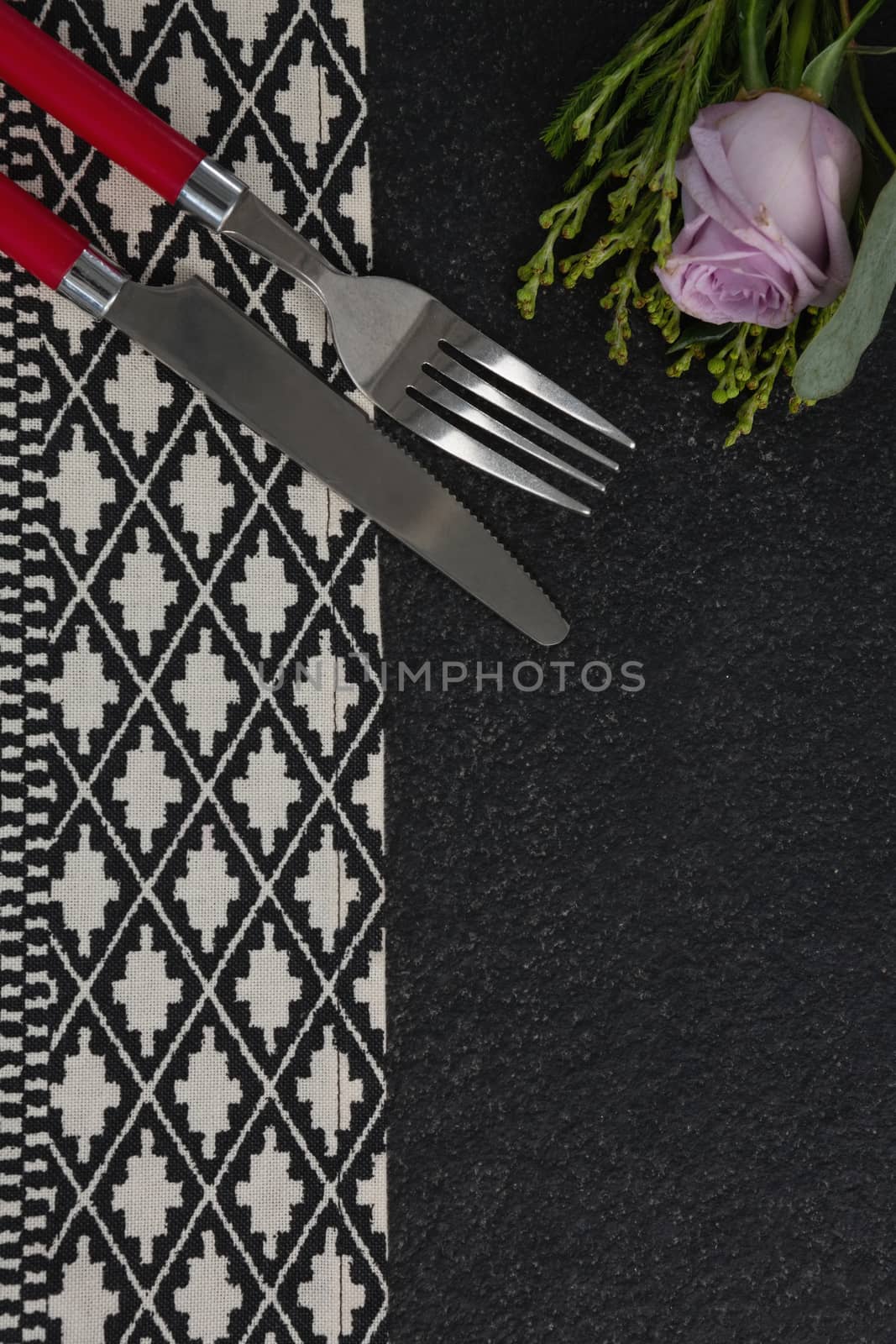 Overhead view of fork and butter knife with rose flower arranged on table cloth