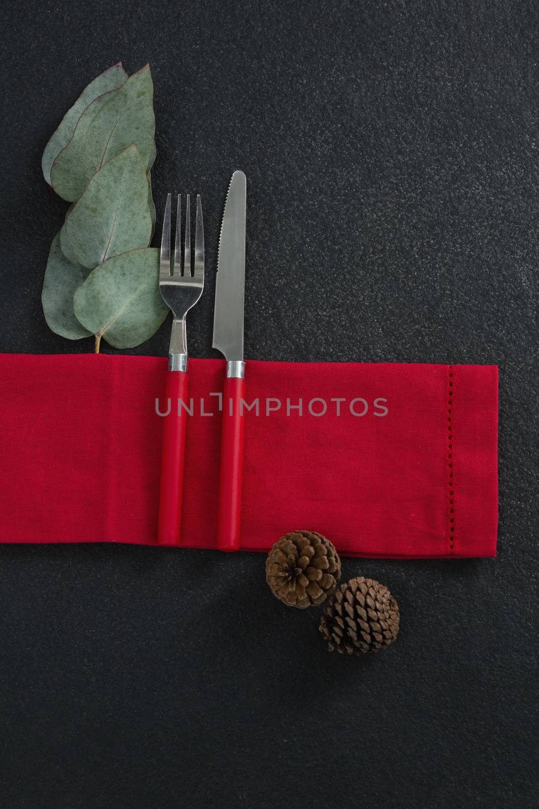 Fork and butter knife with leaf, pine cone and napkin on concrete background