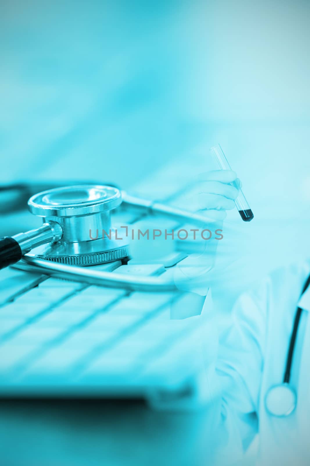 Close-up of keyboard with stethoscope against blond-haired scientist with a mask looking at a test tube