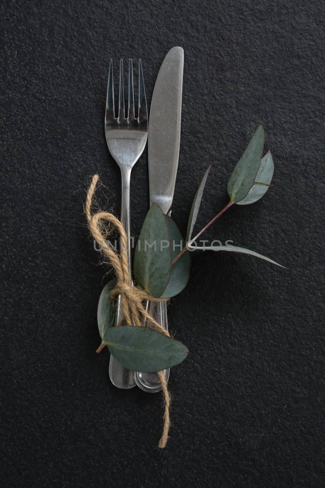 Overhead view of fork, butter knife tied up with leaf on black background