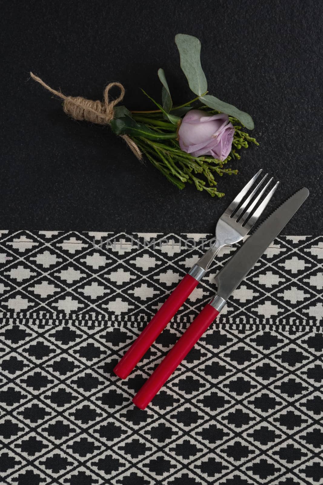 Overhead view of fork and butter knife with rose flower arranged on table cloth
