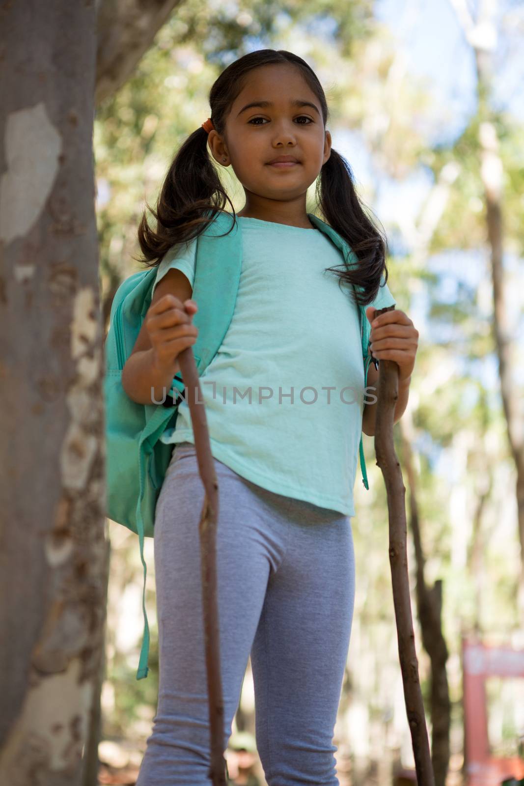 Little girl standing with backpack holding walking sticks in her hands in the forest 