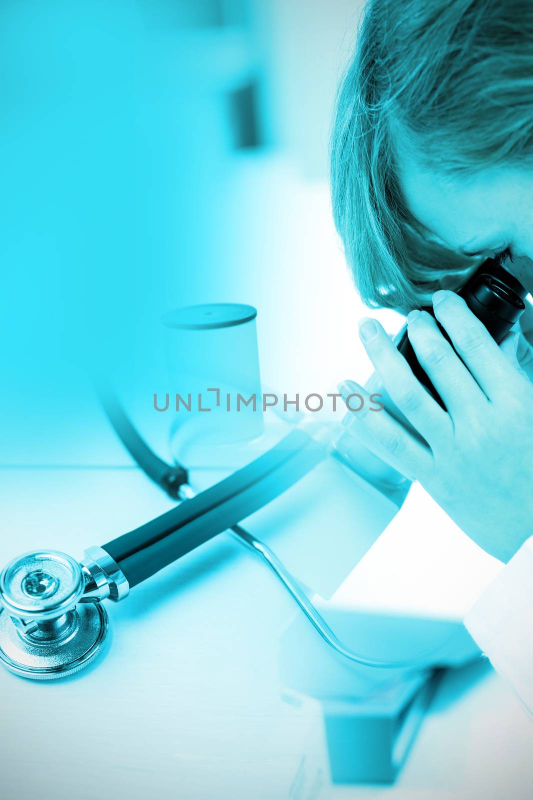 Stethoscope on desk against concentrated female scientist looking through a microscope