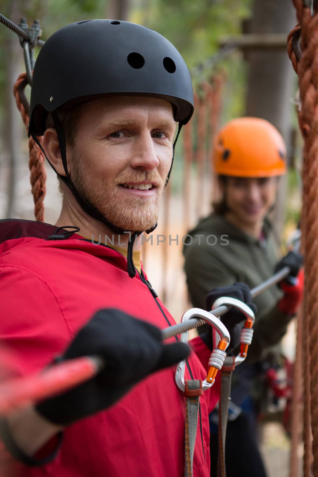 Portrait of smiling young man wearing safety helmet holding zip line cable in the forest