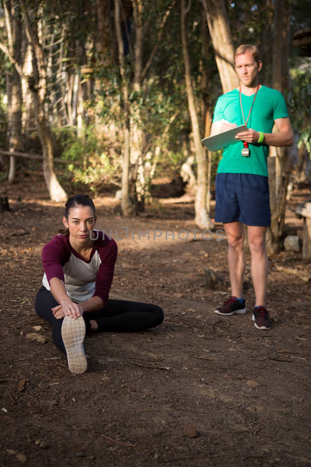 Woman performing stretching exercise with the help of trainer in the forest