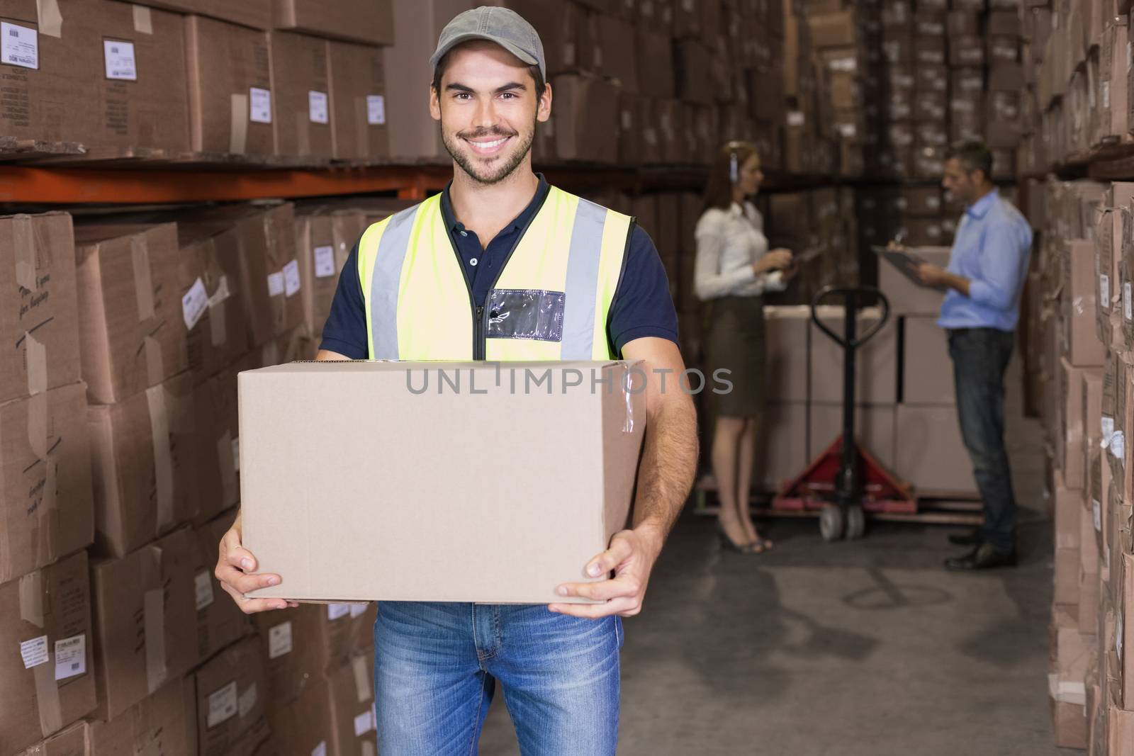 Warehouse worker smiling at camera carrying a box by Wavebreakmedia