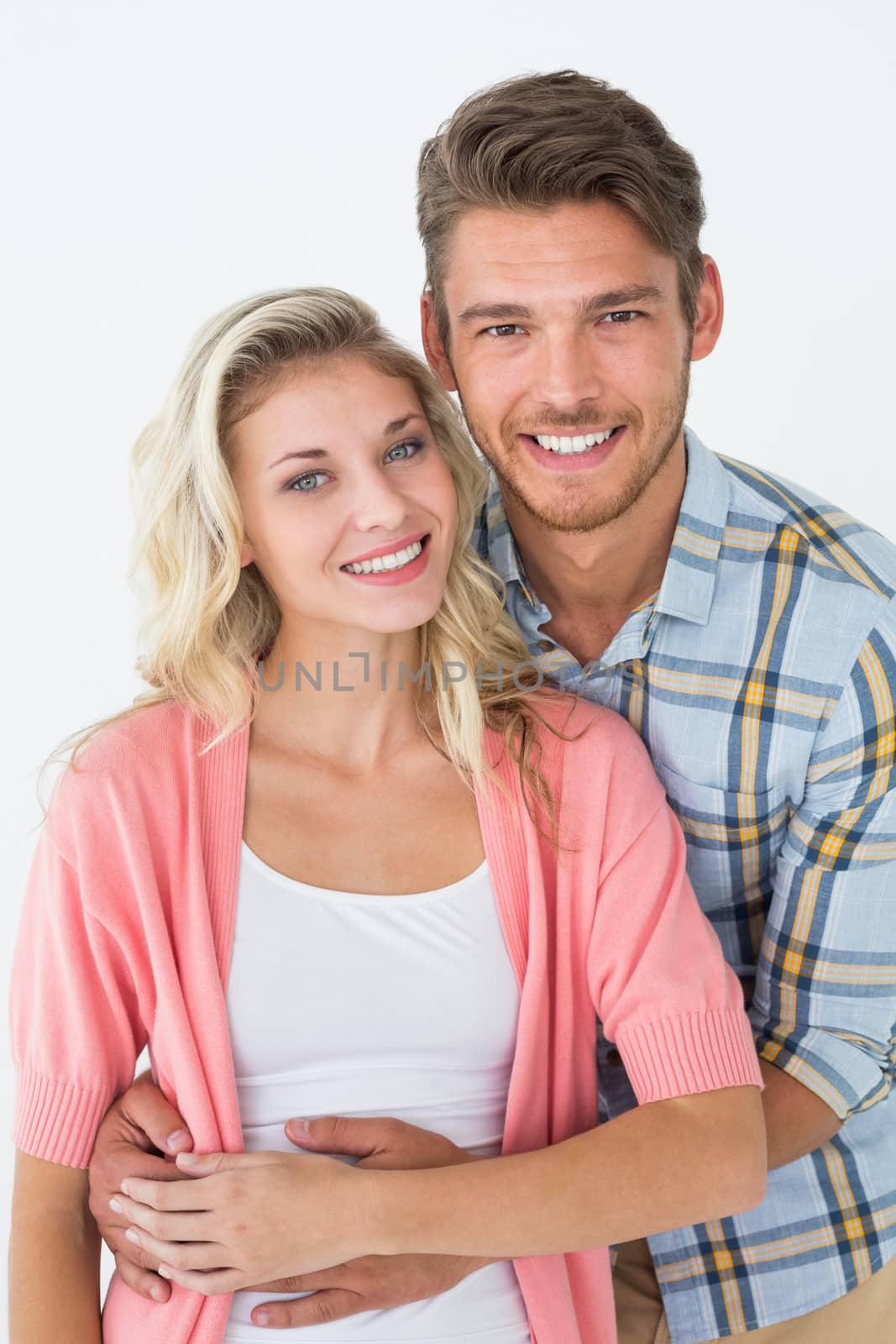 Portrait of young man embracing happy woman from behind over white background