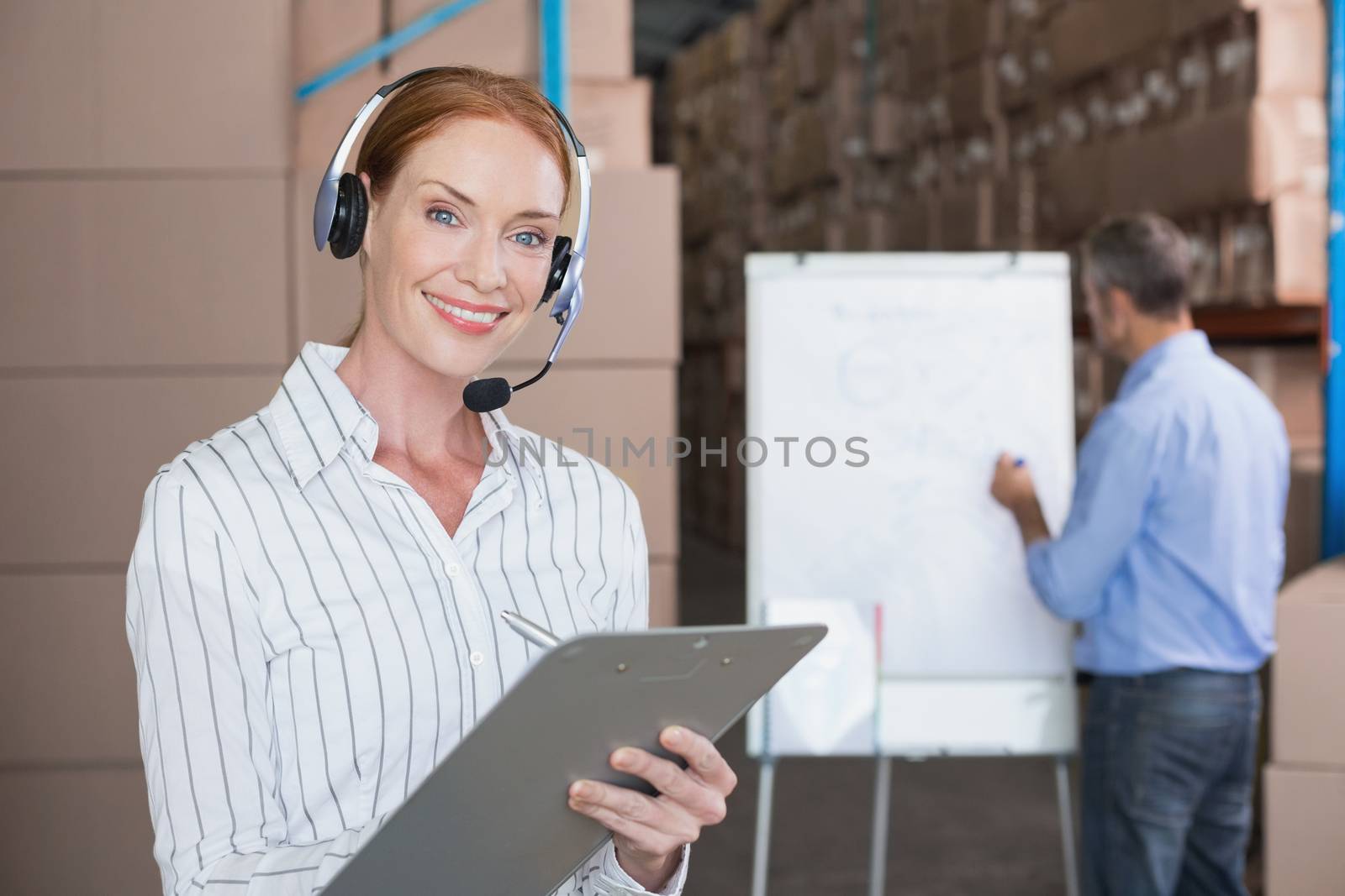 Warehouse manager writing on clipboard in a large warehouse