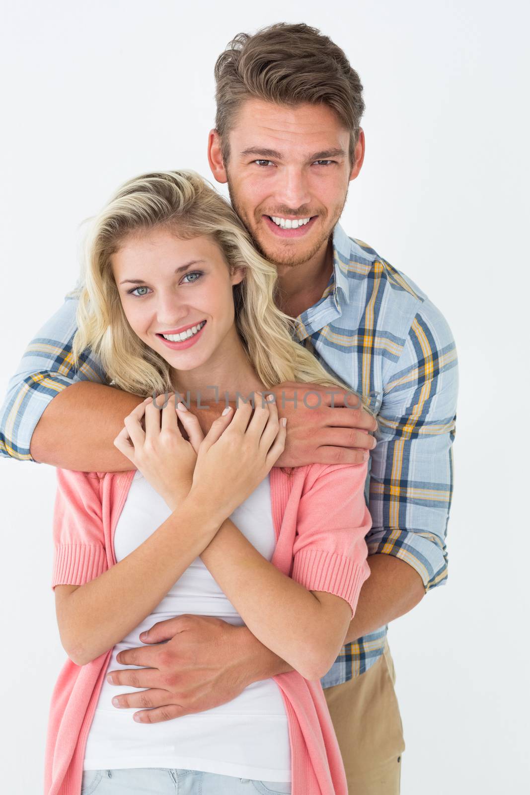 Portrait of young man embracing happy woman from behind over white background