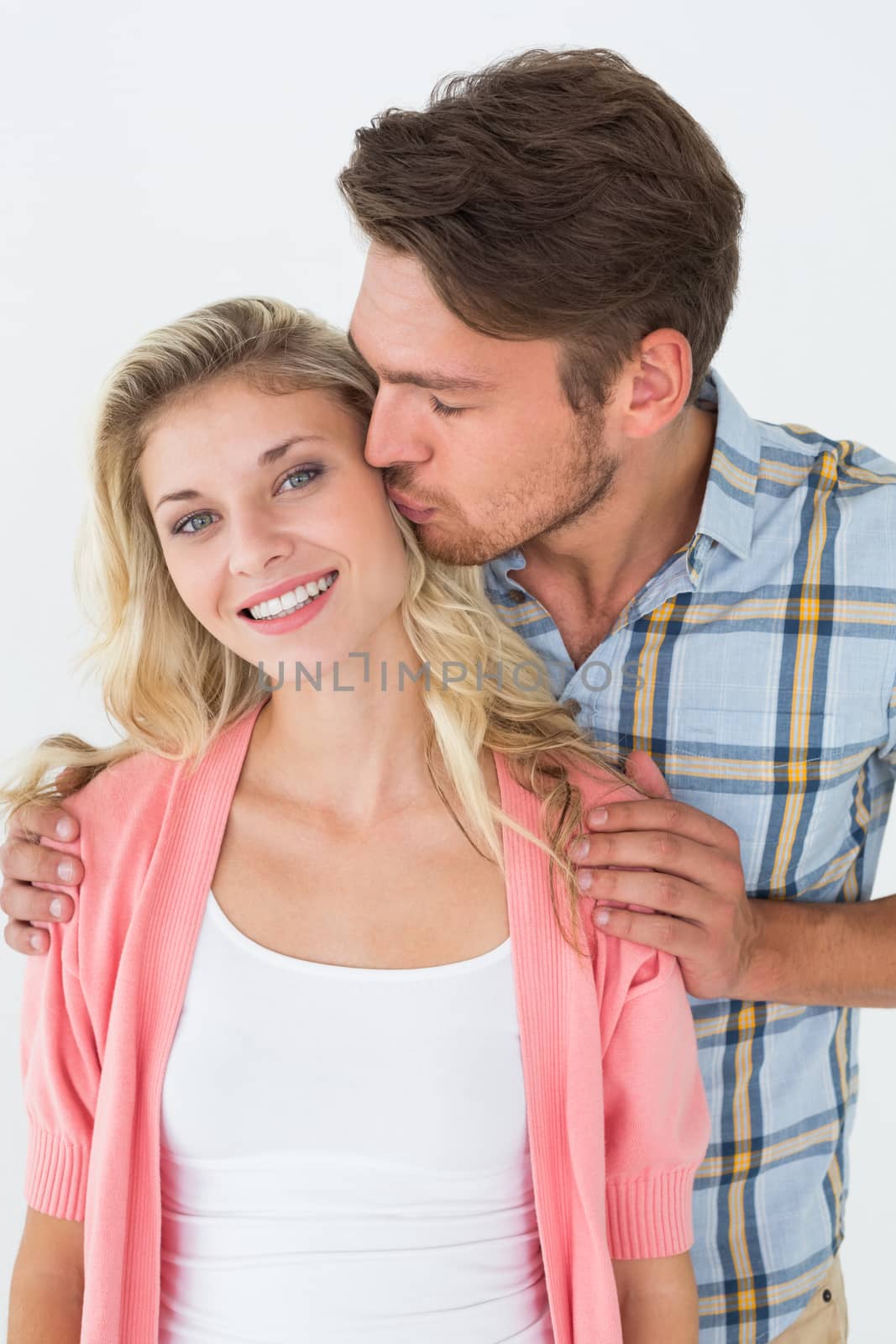 Portrait of young man kissing happy woman over white background