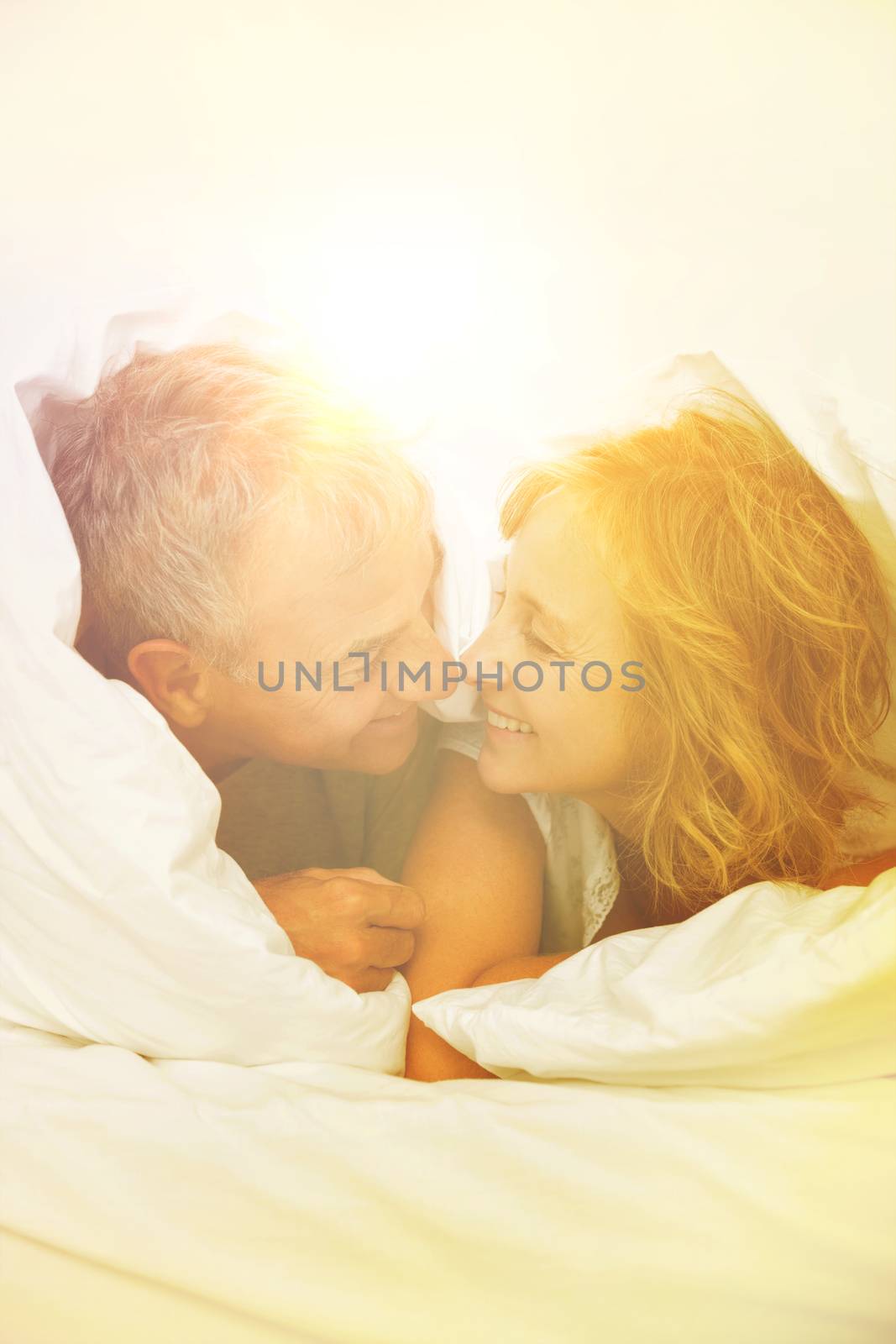 Cute middle aged couple under the duvet in bedroom at home
