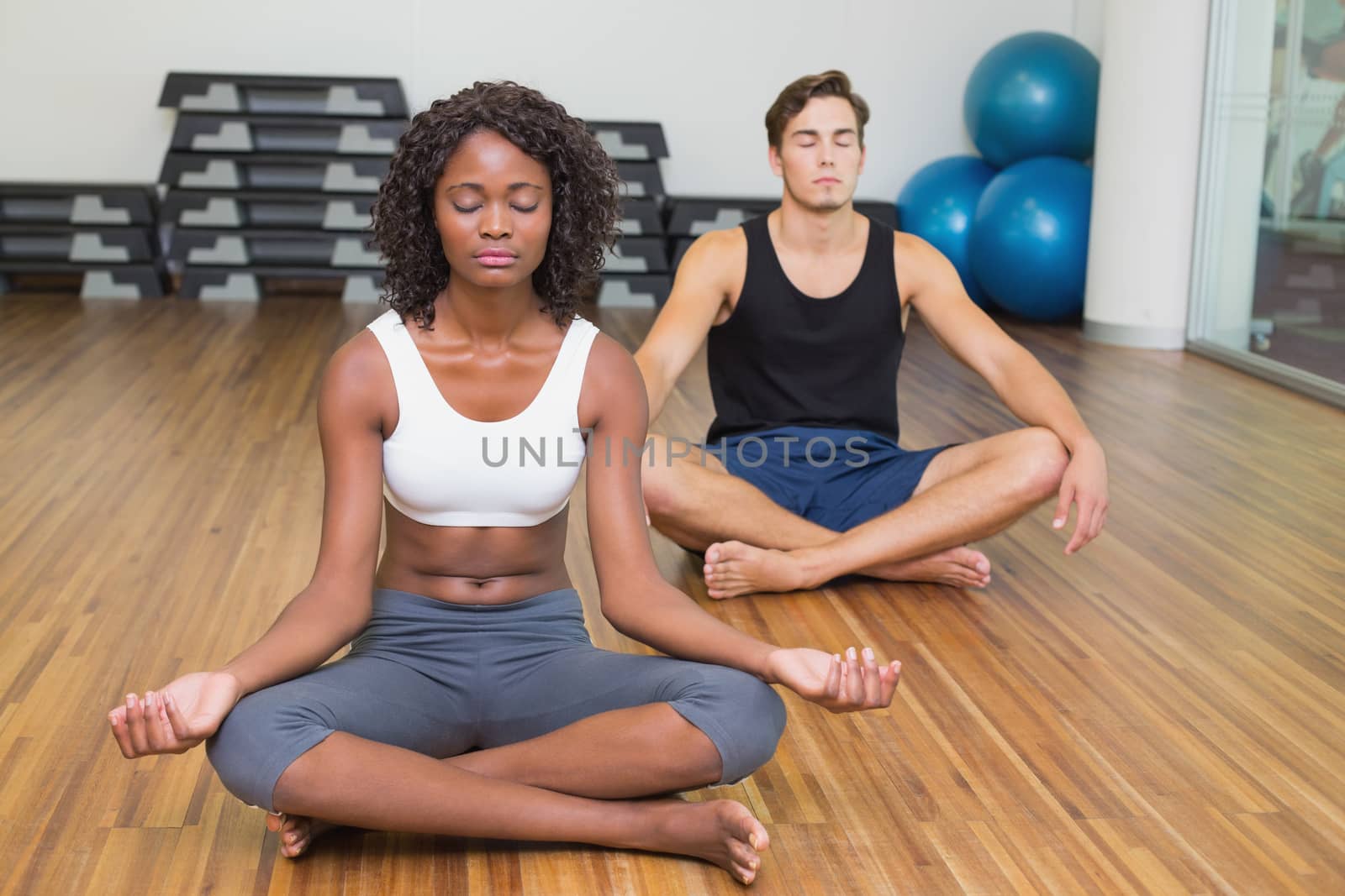 Fit couple sitting in lotus pose in fitness studio at the gym