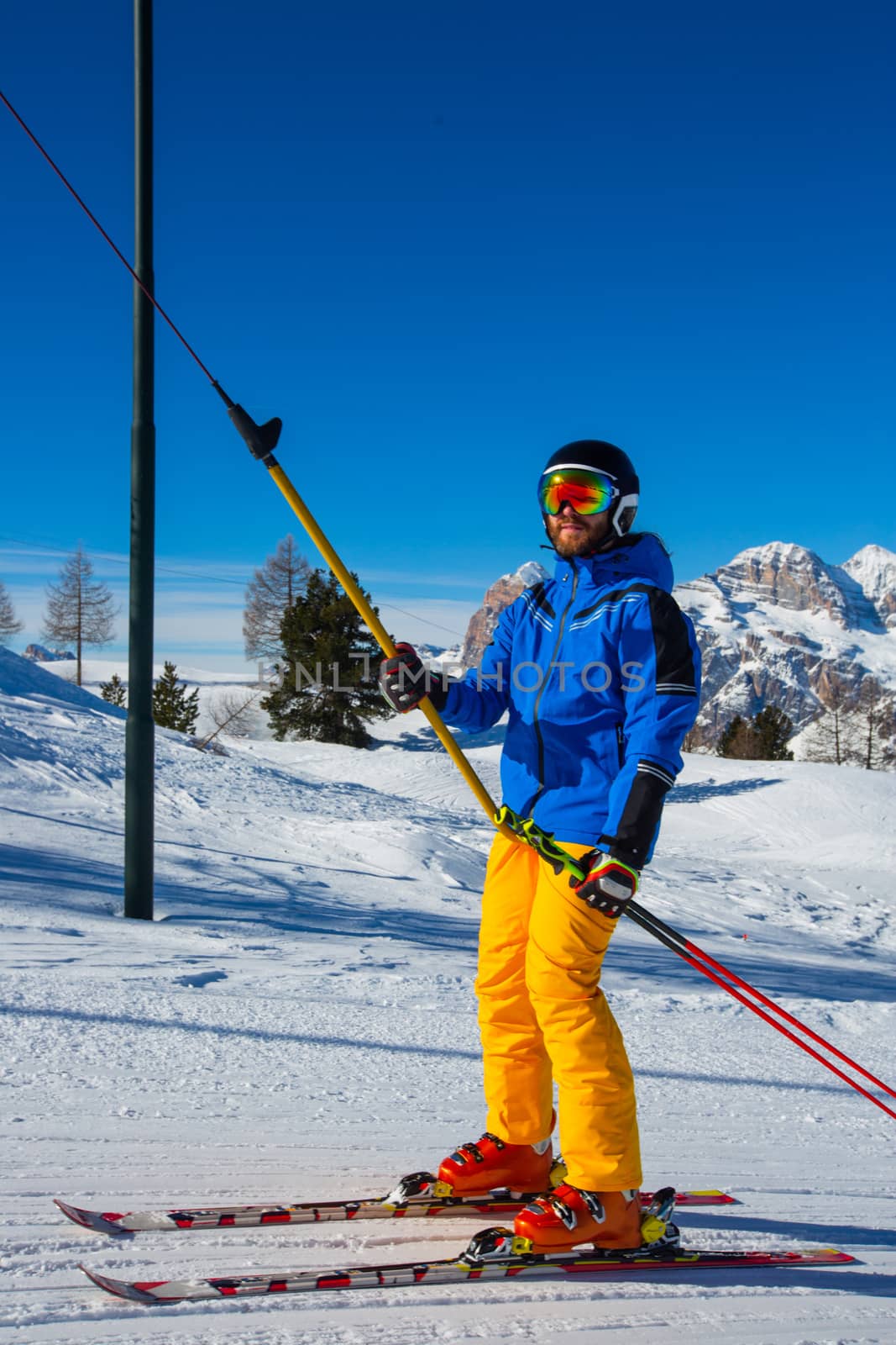 Alpine skier with T-bar lift, blue and yellow clothes on slope with mountains in the background at Cortina d'Ampezzo Faloria skiing resort area Dolomiti Italy