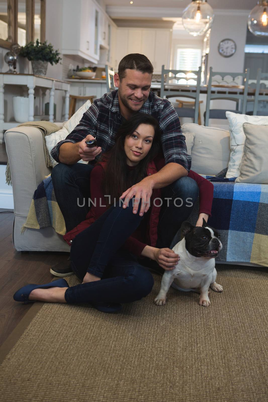 Couple watching television with their pet dog in living room at home