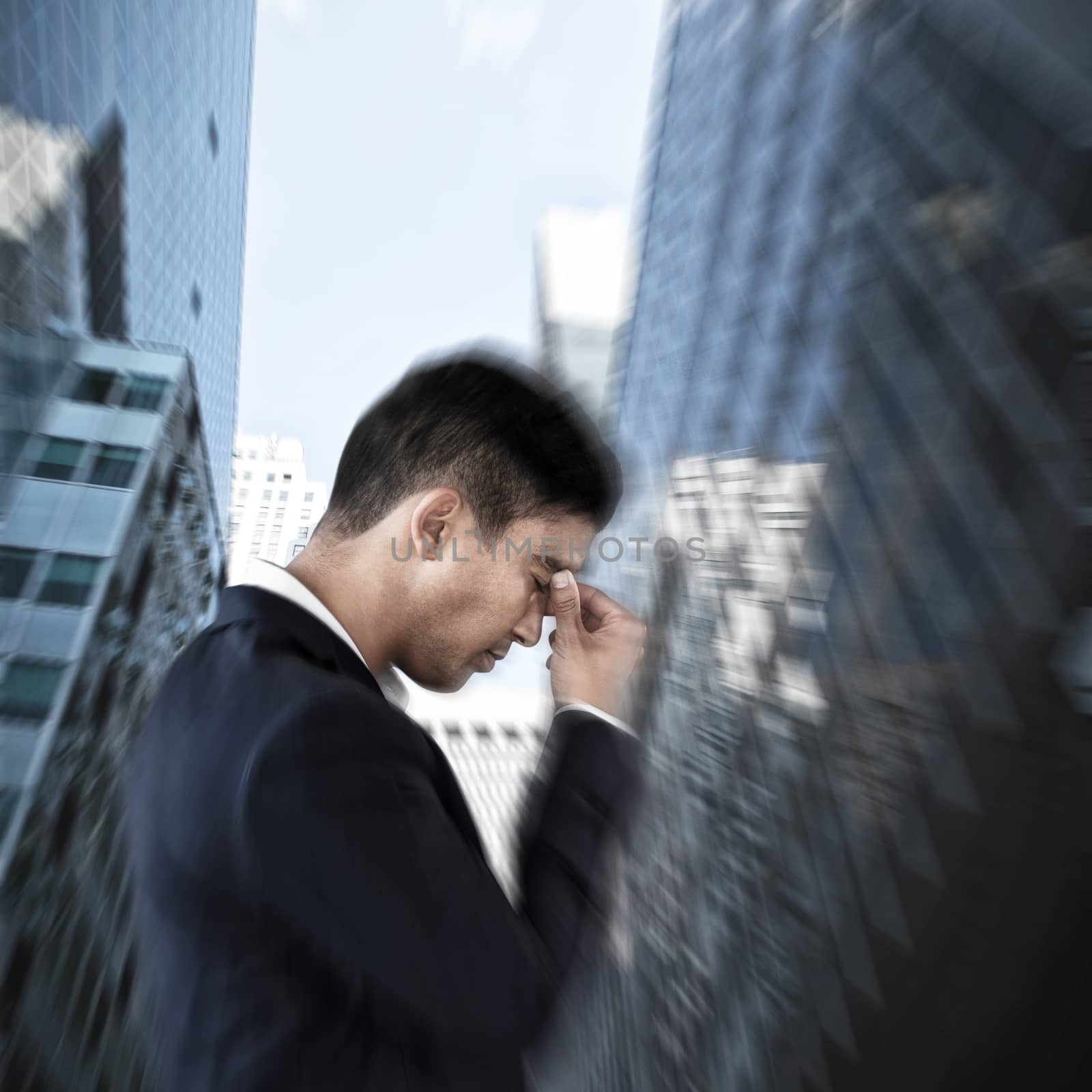 Side view of businessman suffering from headache against low angle view of modern office buildings