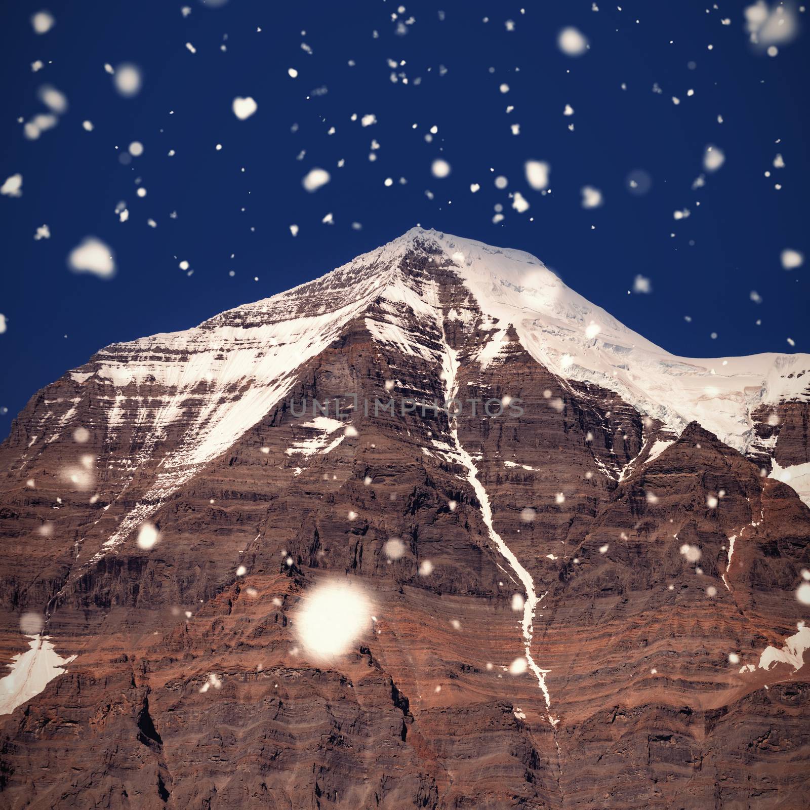 Snow falling against snow capped mountain on a sunny day