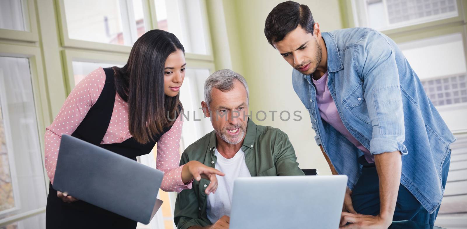 Business people discussing over laptop against glass windows 