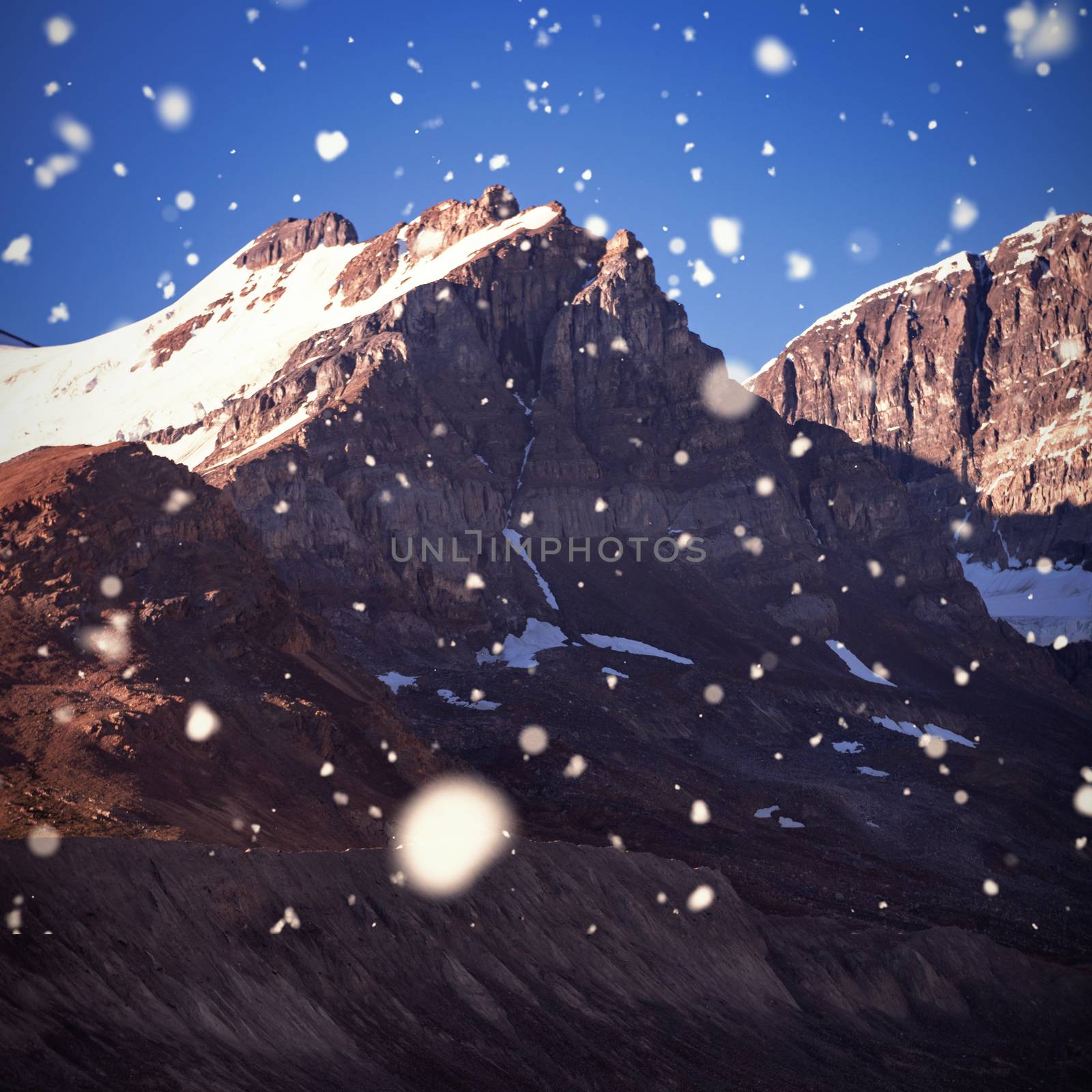 Snow falling against snow capped mountain on a sunny day