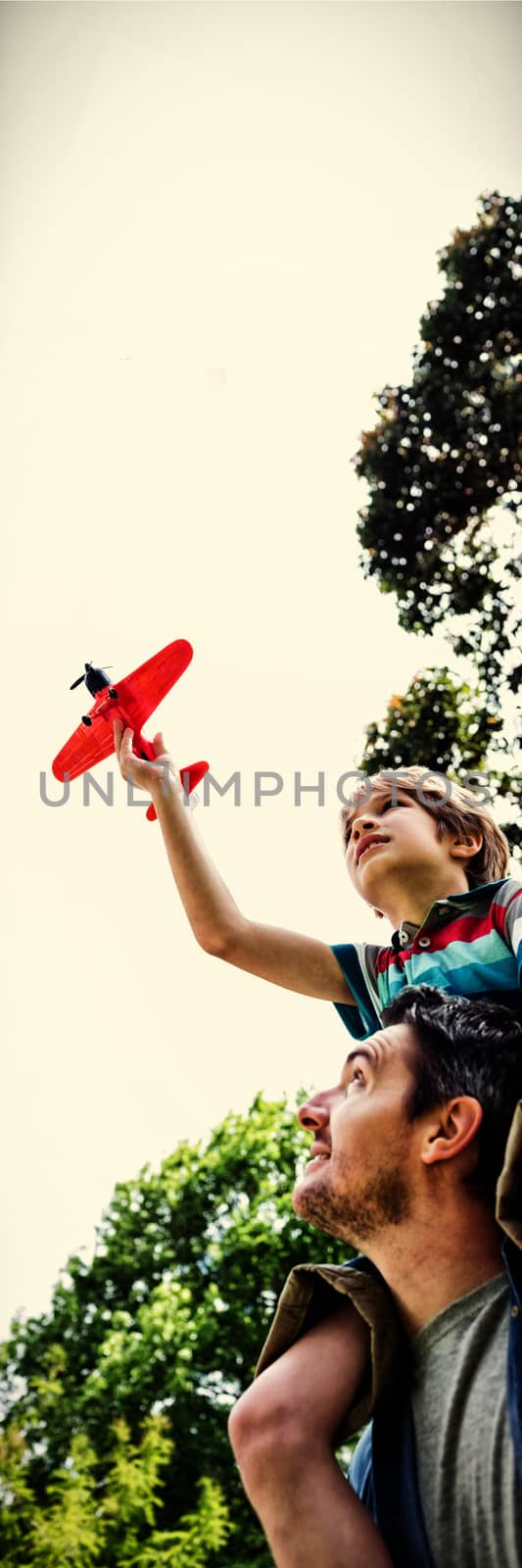 Low angle view of a boy with toy aeroplane sitting on fathers shoulders at the park