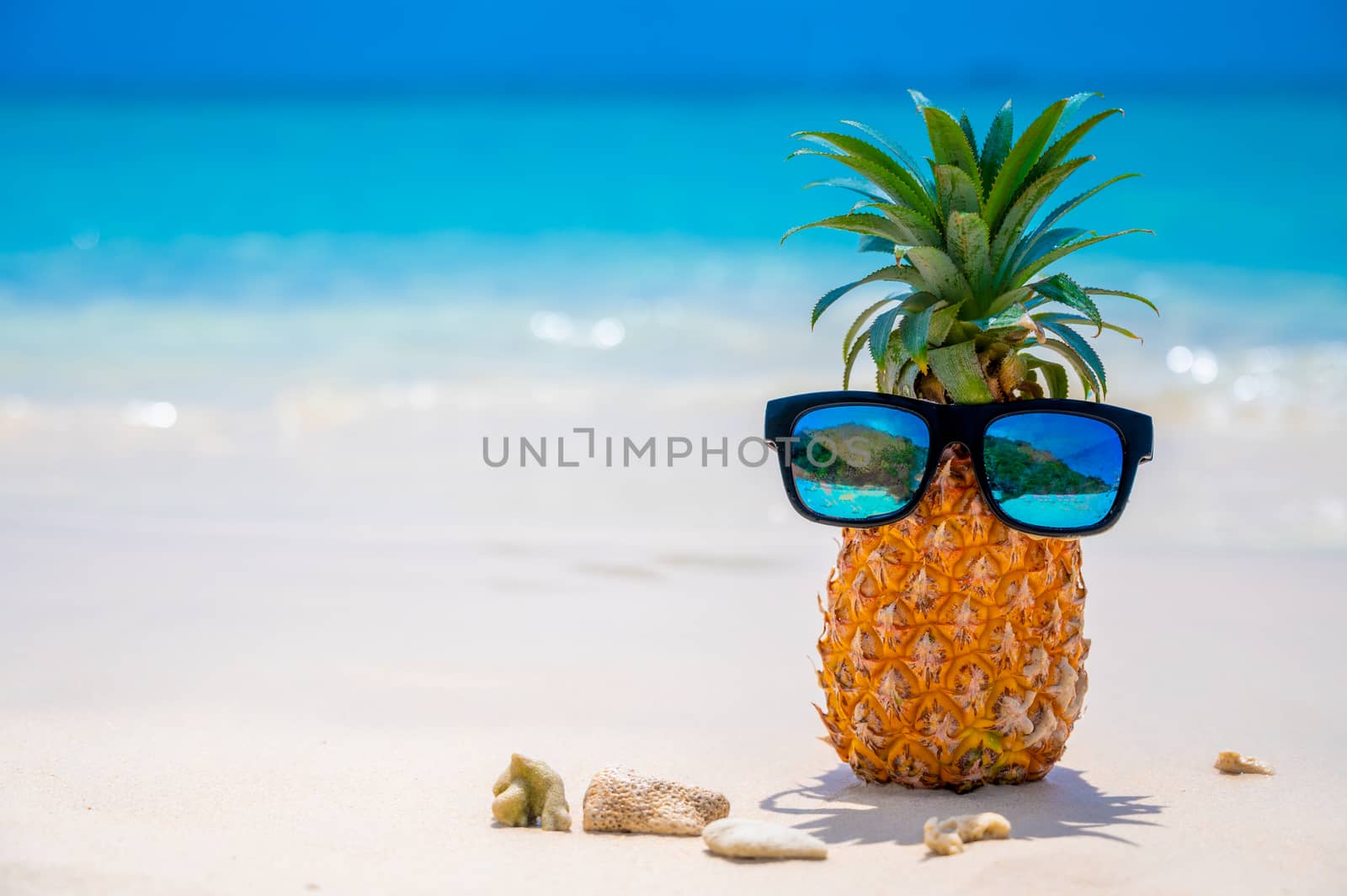 Glasses pineapples are located on the beach by the sea in the hot sun, setting the concept for summer. by sarayut_thaneerat