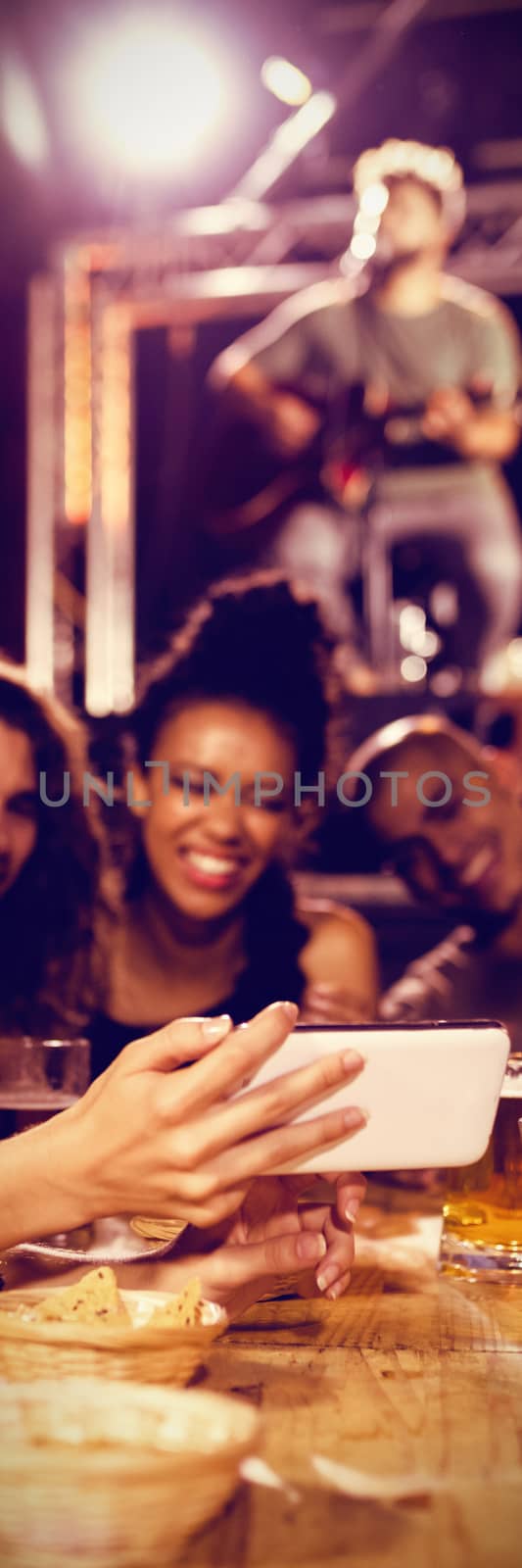 Woman showing smart phone to friends while sitting at table in nightclub