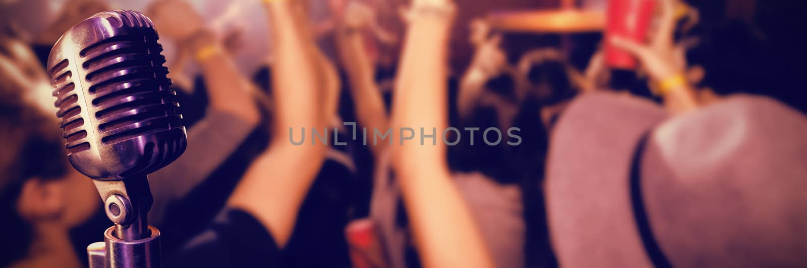 Close-up of microphone  against people with arms raised at nightclub