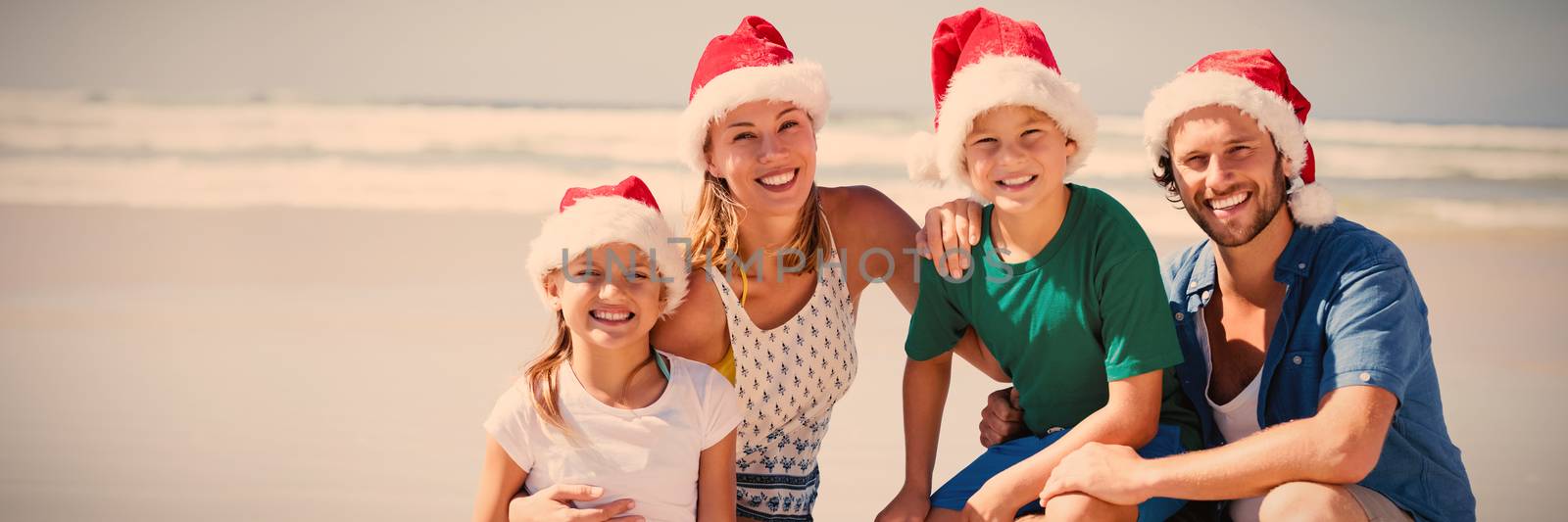 Portrait of smiling family wearing Santa hat at beach by Wavebreakmedia