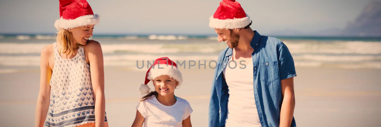 Happy family wearing Santa hat while standing at beach by Wavebreakmedia