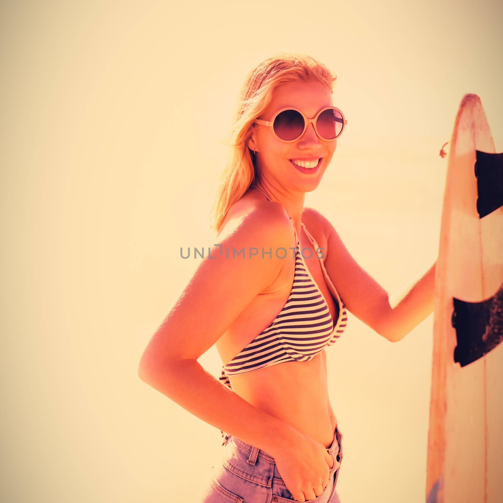 Portrait of smiling young woman holding surfboard at beach during sunny day
