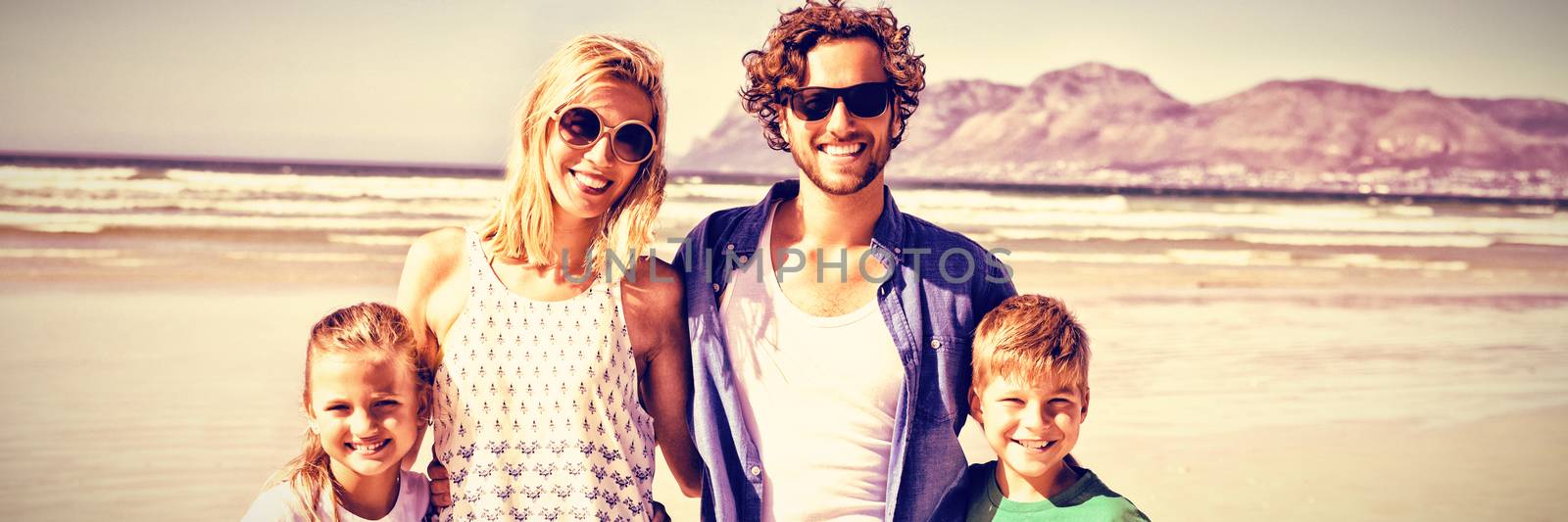 Portrait of happy family standing together at beach during sunny day