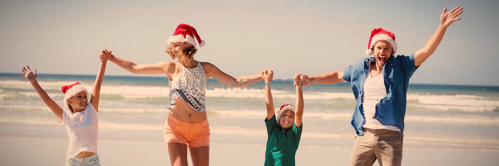 Cheerful family wearing Santa hat while jumping at beach by Wavebreakmedia