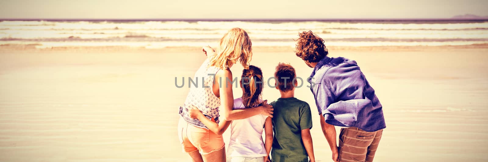 Rear view of family standing together on shore at beach during sunny day