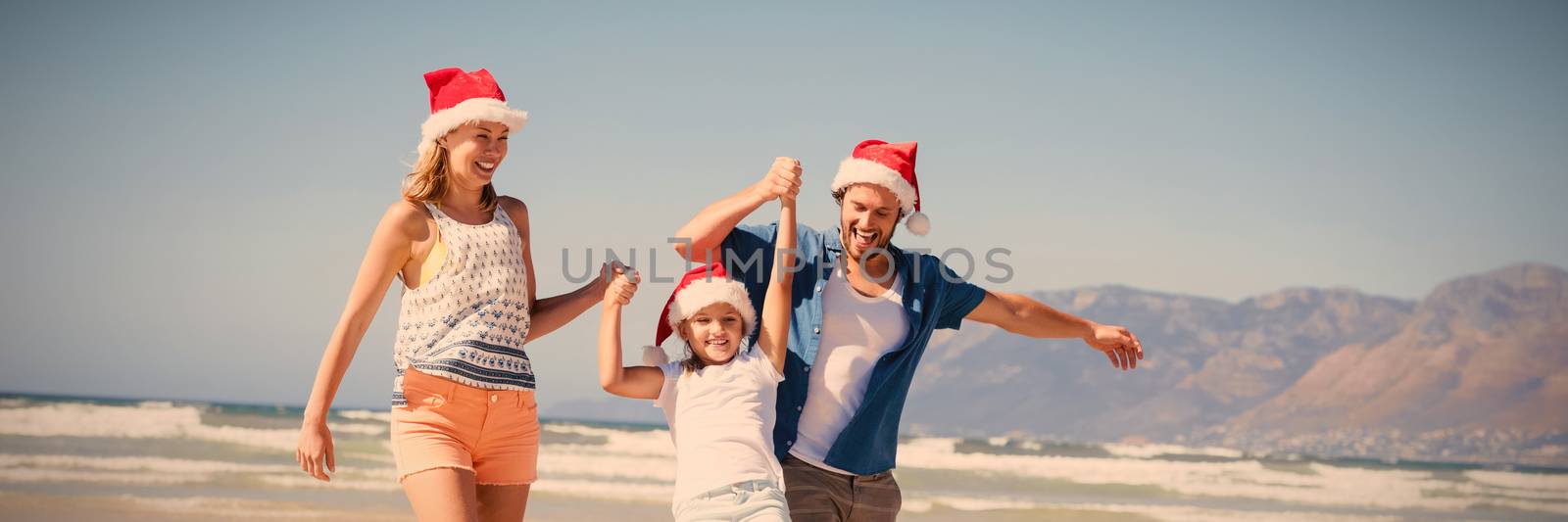 Happy family wearing Santa hat while enjoying at beach during sunny day