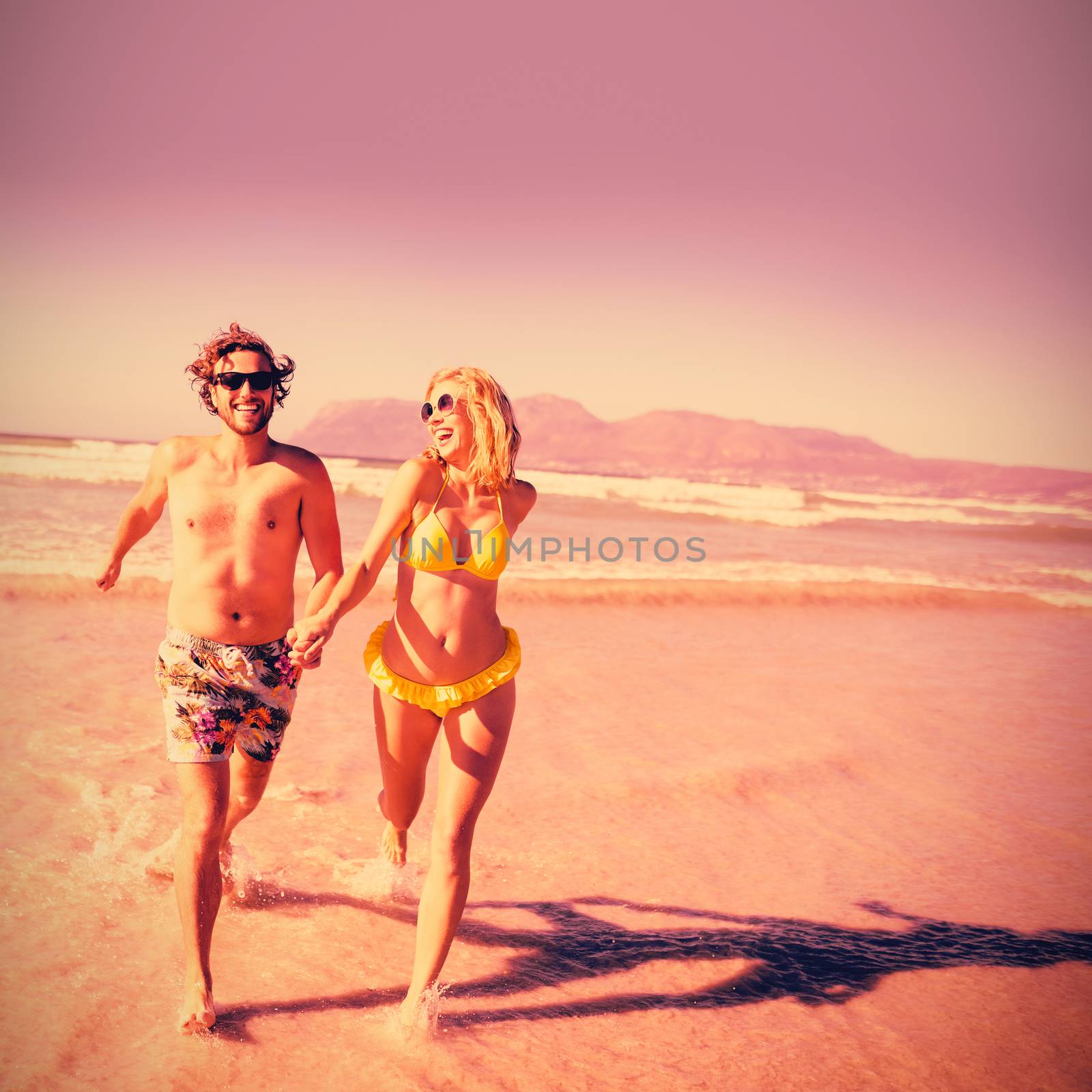 Happy couple holding hands while running on shore at beach during sunny day