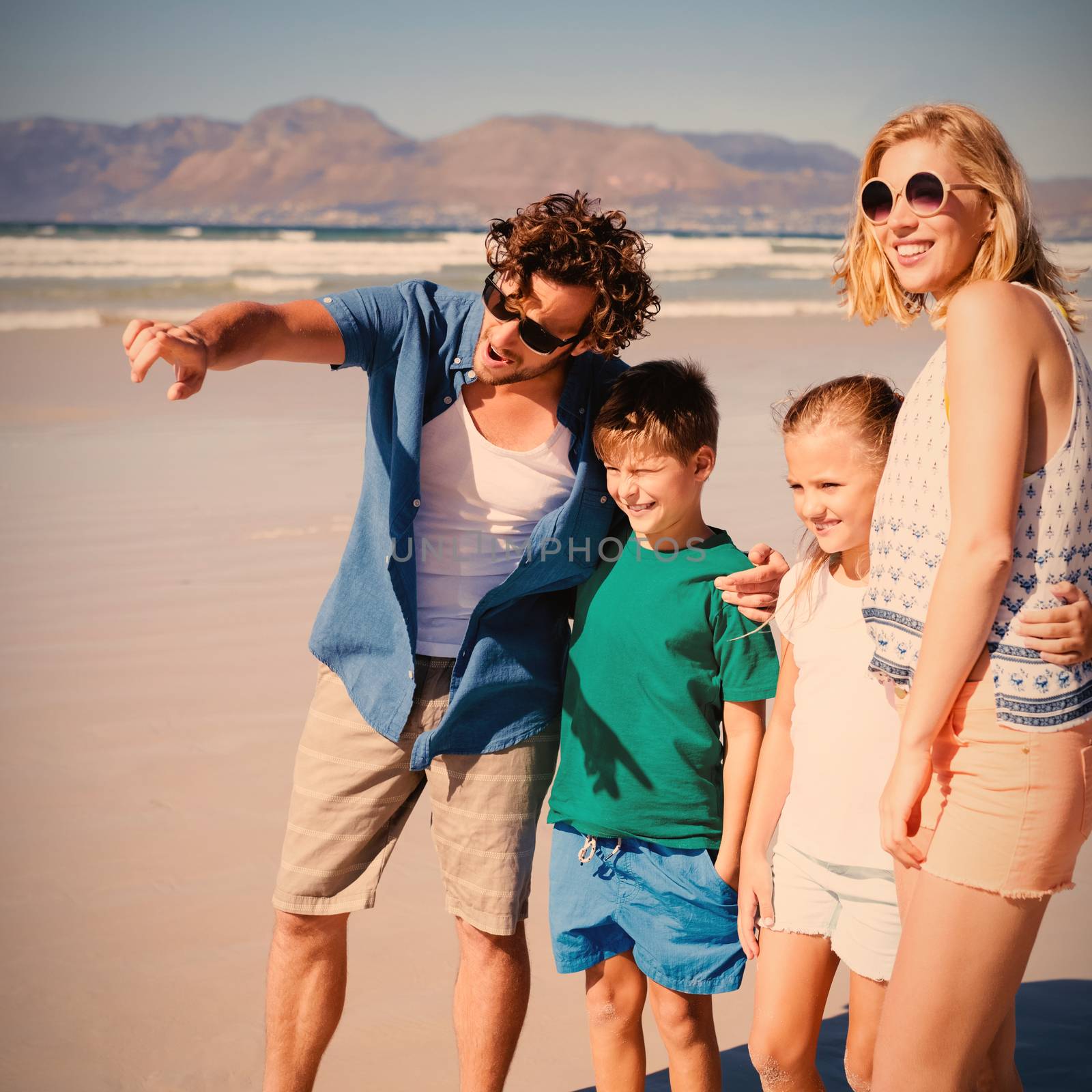Man pointing away with family standing at beach by Wavebreakmedia