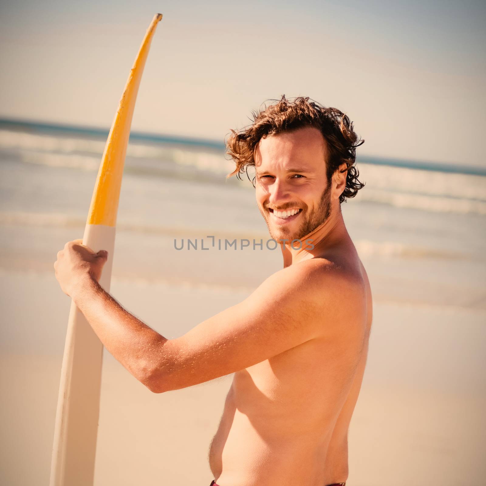 Portrait of happy shirtless man holding surfboard at beach during sunny day