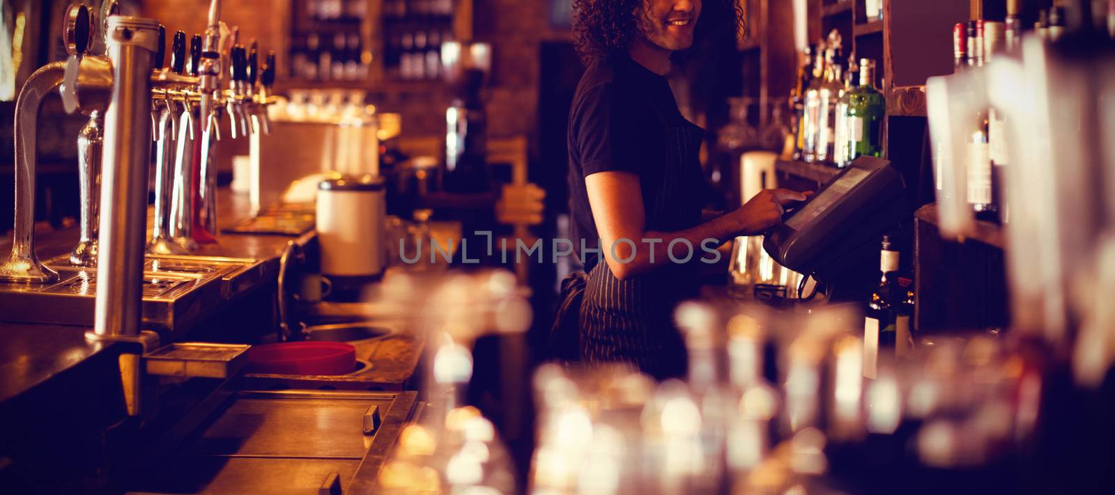 Young waiter using a electronic machine in pub
