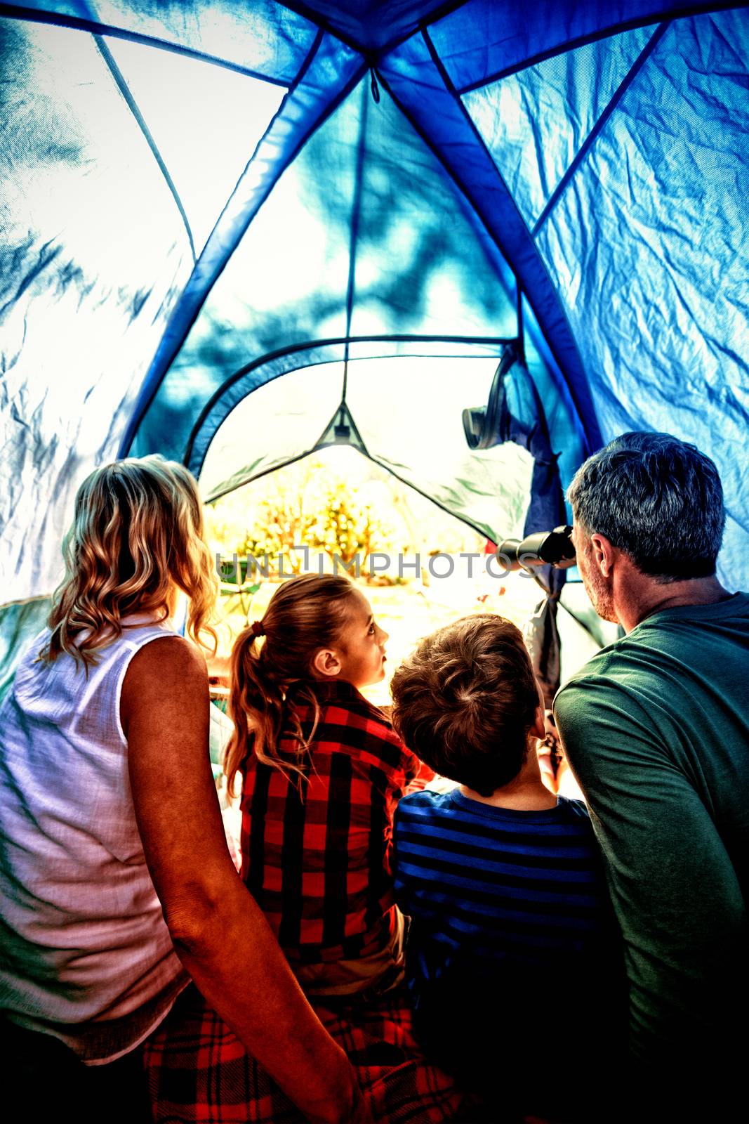 Rear view of family looking through telescope while sitting in the tent