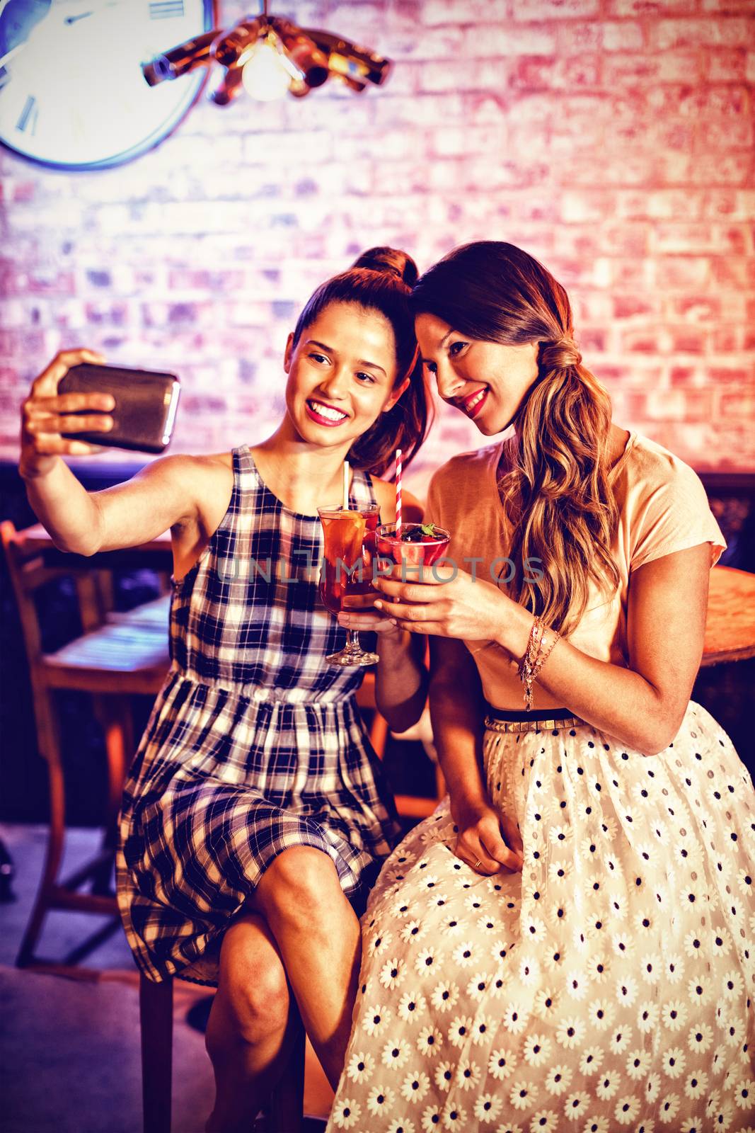 Young women taking a selfie while having cocktail drinks in pub