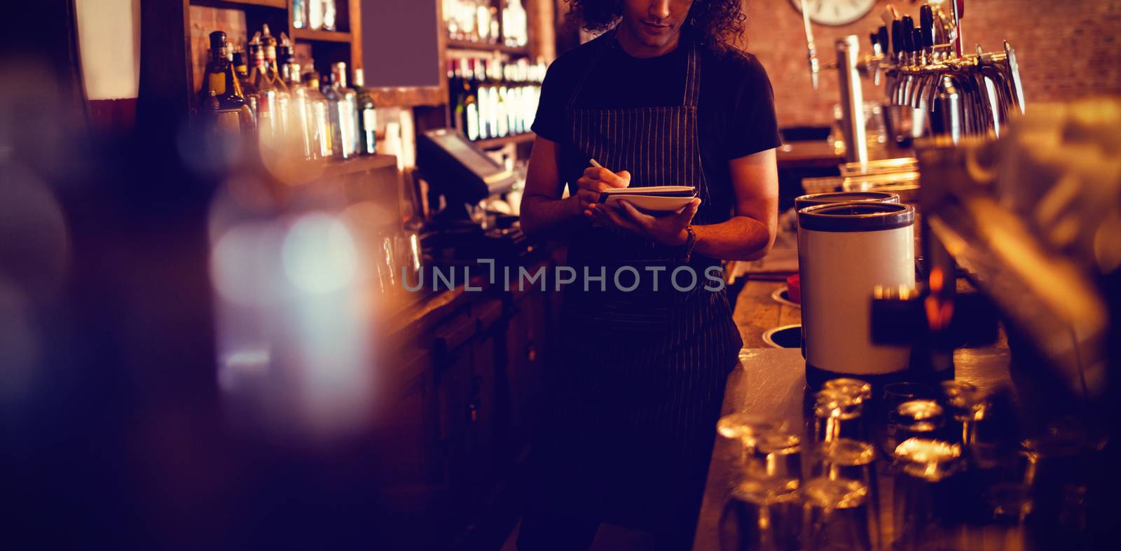 Young waiter writing on diary in pub