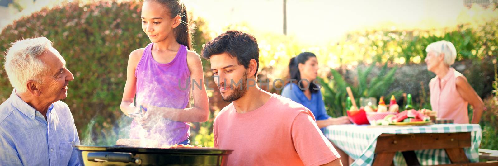 Father and grandfather watching while girl preparing barbecue in the park