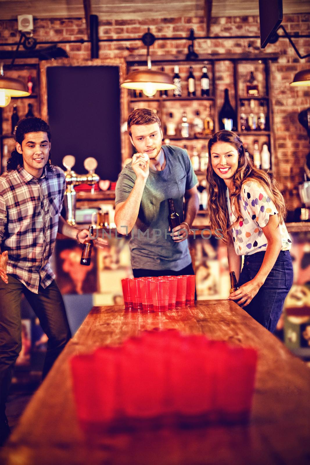 Group of happy friends playing beer pong game  by Wavebreakmedia