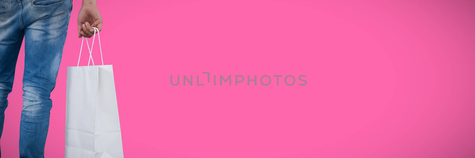 Mid section of man carrying shopping bag against pink background