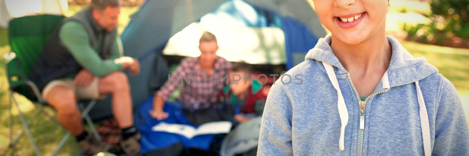 Girl smiling at camera while family sitting at tent in background on a sunny day