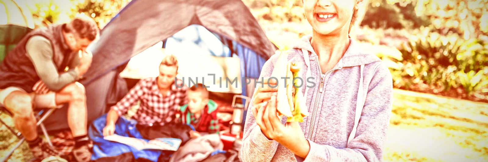 Portrait of smiling girl holding a sandwich while family sitting outside the tent