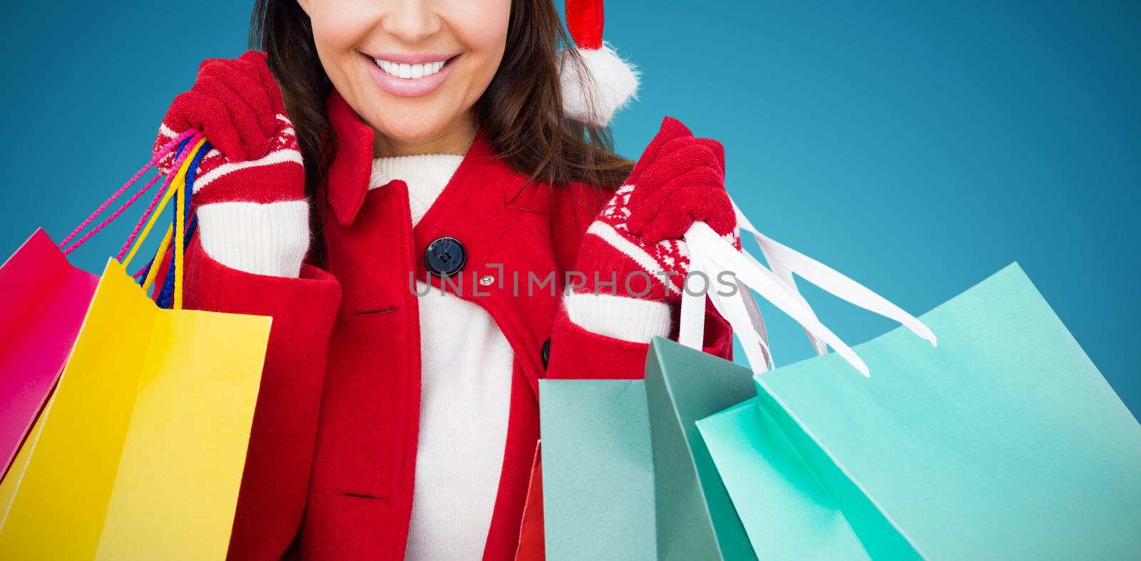 Beautiful brunette with santa hat holding shopping bags against abstract blue background