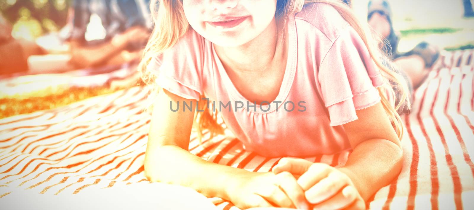 Portrait of smiling girl lying on blanket and reading book while family sitting in background